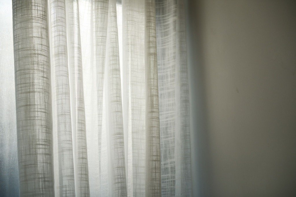 Sheer white curtains gently lit by daylight create subtle shadows on the wall, curtains vs blinds in Cairo
