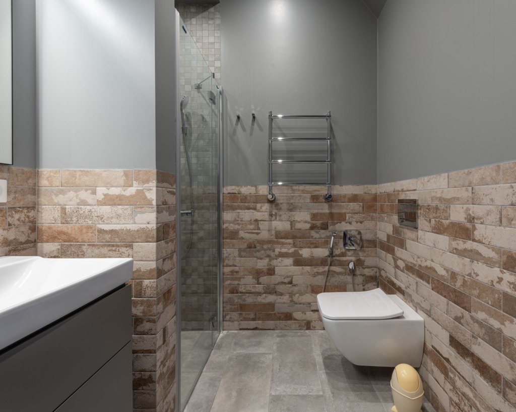 Stylish contemporary bathroom featuring a glass shower and brick accent wall, flooring for a New Cairo apartment