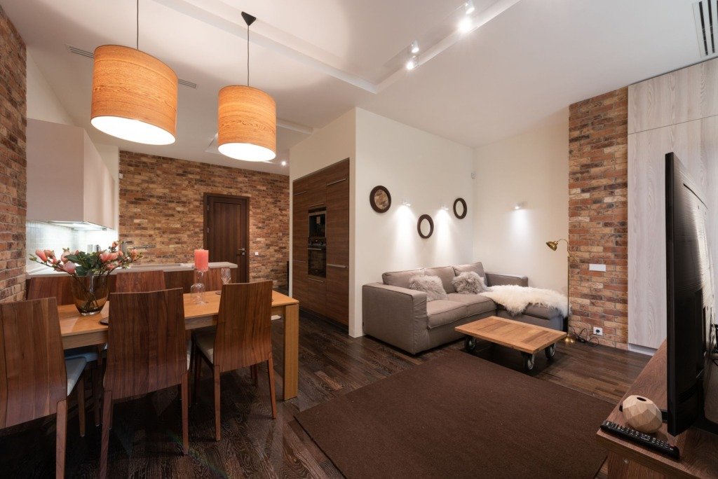 Modern apartment interior with dining table and chairs decorated with candles and flower vase with lamps on ceiling near cabinets and couch with pillows near TV and coffee table