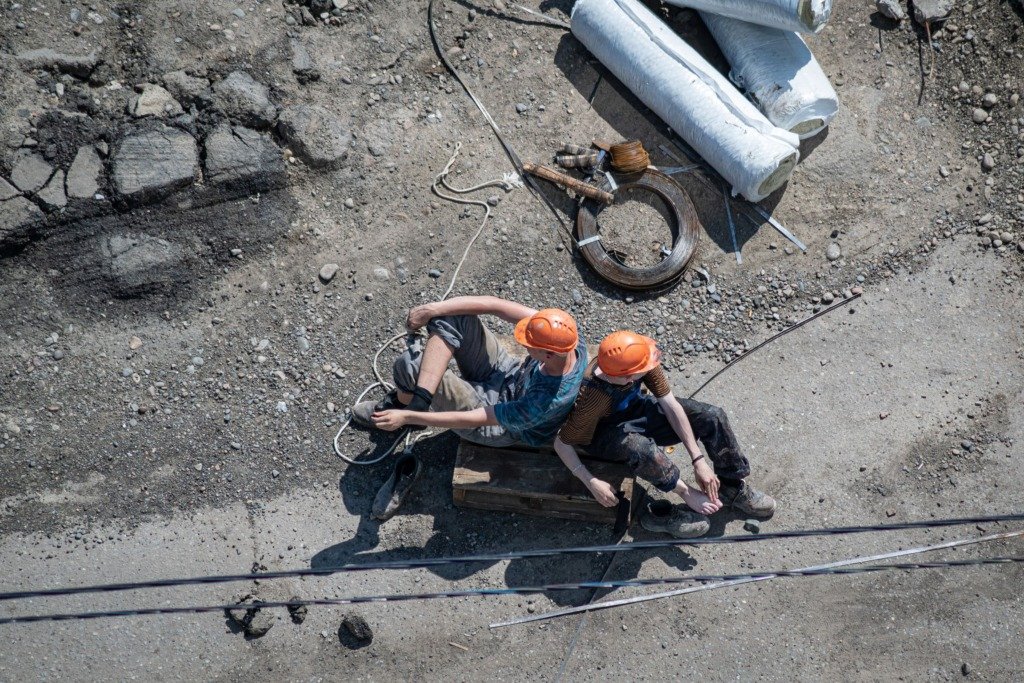 Two construction workers in hard hats rest on a site, viewed from above.