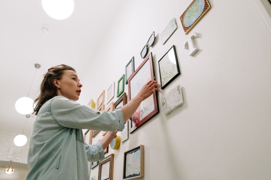 A woman arranging picture frames on a bright indoor wall.