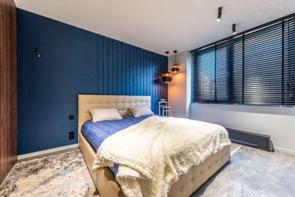 Plaid with pillows on bed against lamps and window blinds above tiled floor in contemporary bedroom, warm vs cool lighting in Cairo
