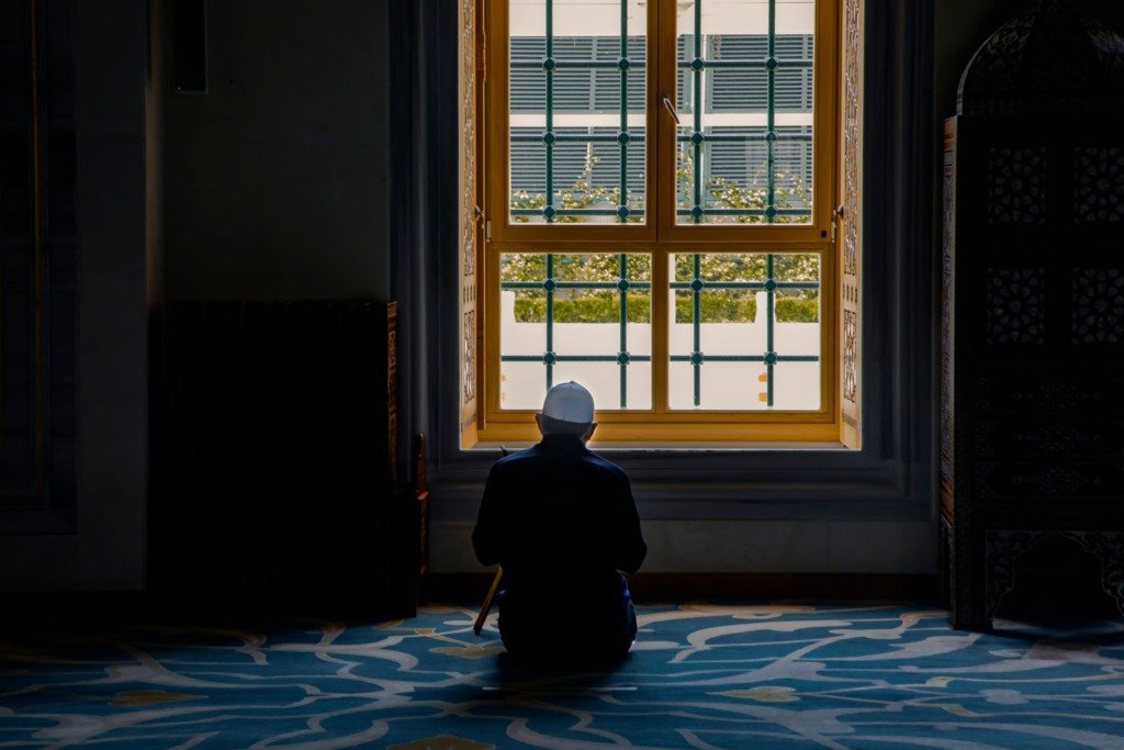 Person in silhouette kneeling in a peaceful interior space by a large window, exuding tranquility and contemplation.