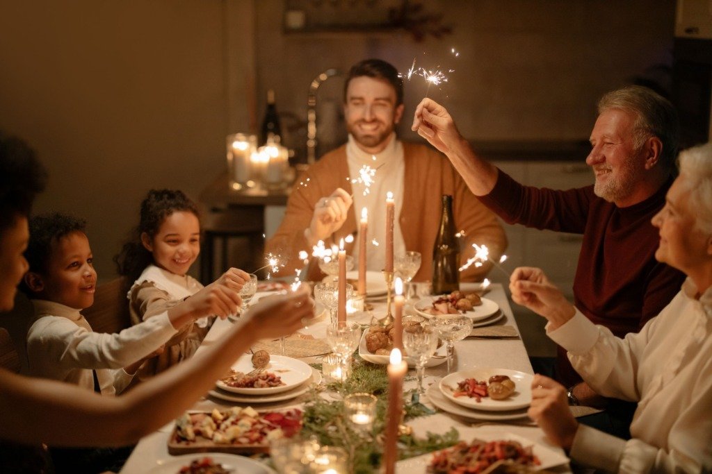Family gathered around a dining table celebrating with sparklers, candles, and a meal indoors.