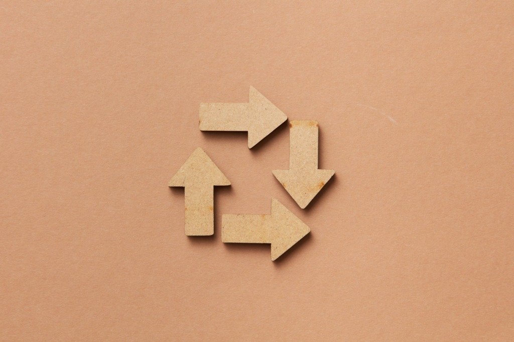 Close-up of a recycling symbol made from wooden arrows on a beige background.