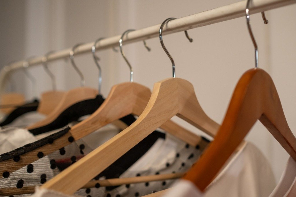 Close-up of wooden clothes hangers with assorted clothing indoors.